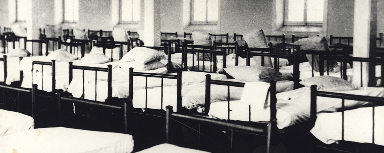 A imagem, em preto e branco, mostra o dormitório da Hospedaria de Imigrantes do Brás, com inúmeras camas posicionadas lado a lado