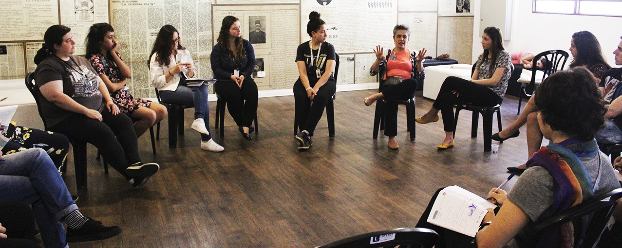 A imagem mostra mulheres, sentadas em roda, conversando em uma sala