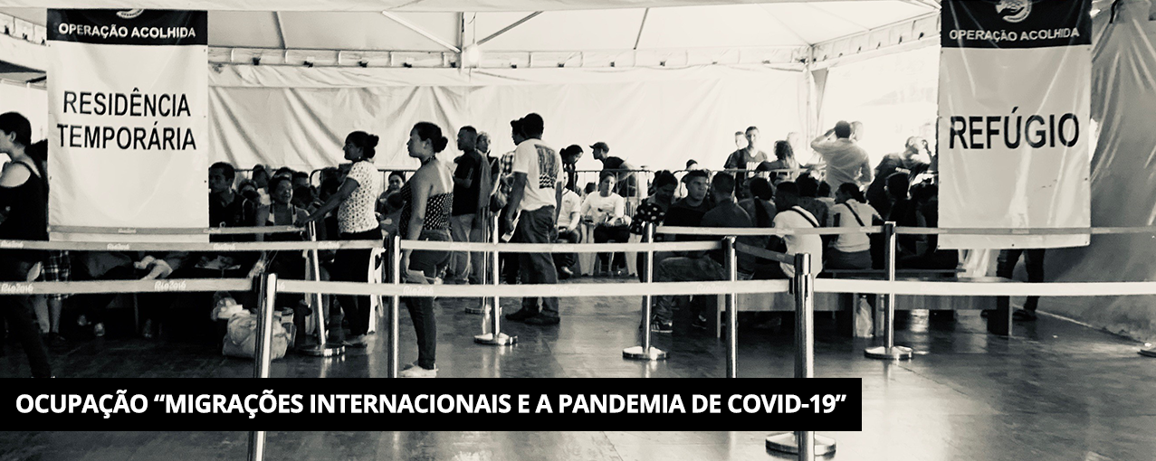 Em preto e branco, mostra, dentro de tenda, pessoas esperando atendimento na Operação Acolhida. Tarja preta com Ocupação "Migrações Internacionais e a pandemia de COVID-19" escrito em branco